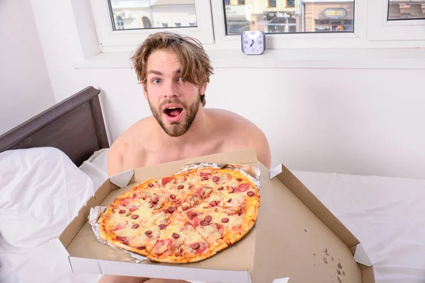 Service de livraison de nourriture. Homme barbu beau gars manger de la nourriture au fromage pour le petit déjeuner au lit. L'homme aime la pizza pour le petit déjeuner. Qui se soucie de l'alimentation. Guy tient une boîte à pizza assis lit dans la chambre ou la chambre d'hôtel — Photo