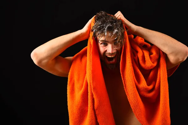 Wash off foam with water carefully. Man with orange towel wipe hair. Apply conditioner after shower. Macho attractive nude guy black background. Man bearded tousled hair covered with foam soap suds