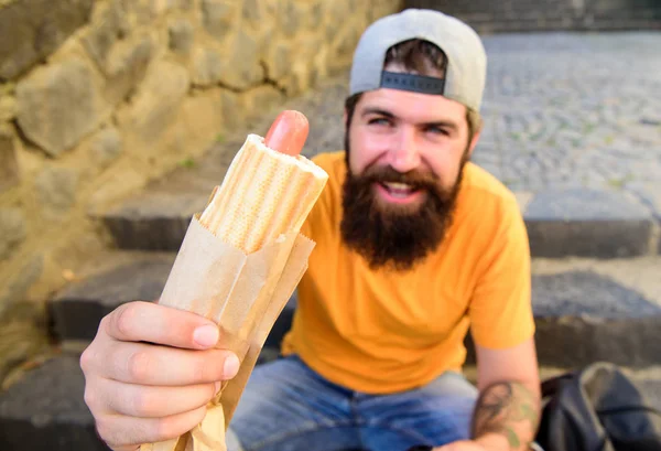 Salsicha de cachorro-quente saborosa em pão torrado. Aproveite o seu conceito de refeição. Conceito de cultura alimentar urbana. Hipster comer cachorro-quente enquanto se sentar em escadas ao ar livre. Homem barbudo hipster desfrutar de comida de rua fundo urbano — Fotografia de Stock