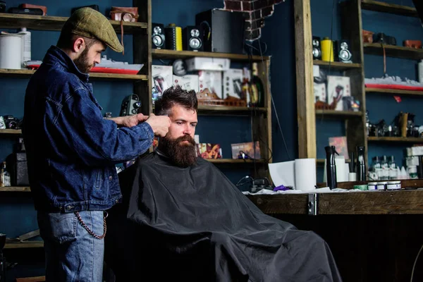 Um cliente Hipster a cortar o cabelo. Barbeiro com cortador de cabelo trabalhar no penteado para hipster, barbearia fundo. Barbeiro com clipper aparar o cabelo no templo do cliente barbudo. Conceito de estilo de vida Hipster — Fotografia de Stock