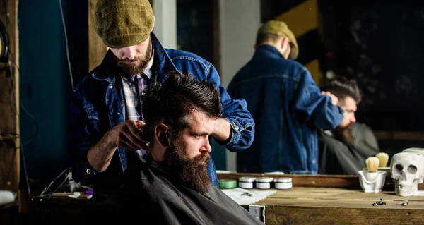 Um cliente Hipster a cortar o cabelo. Cabelo de barbeiro styling de cliente barbudo com pente e cortador. Conceito de corte de cabelo. Barbeiro com cortador de cabelo funciona no penteado para homem com barba, barbearia fundo — Fotografia de Stock