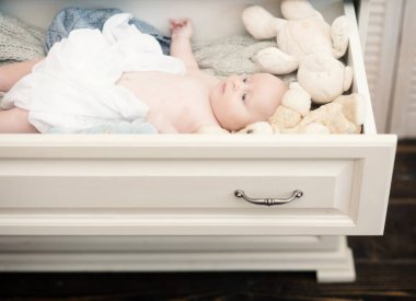 Yeni doğan bebek mavi gözleri ve merak yüz. Beyaz ahşap göğüs çekmecede yalan bebek