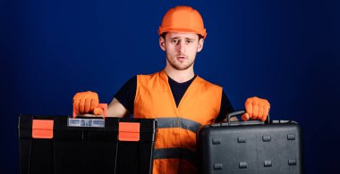 İşçi, repairer, tamirci, Oluşturucu düşünceli yüzündeki iş için ekipman seçimi. Araç ve ekipman kavramı. Araç kutusu ve araç, mavi arka plan ile bavul kask, kask içinde adam tutar.