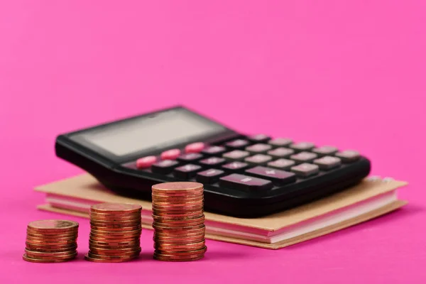 Montones de monedas y calculadora para la planificación del presupuesto. Calculadora en cuaderno con dinero al lado sobre fondo rosa —  Fotos de Stock