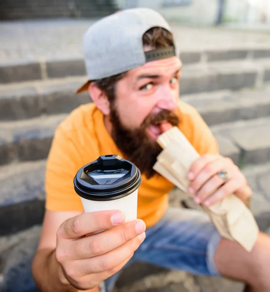 Hipster morso hot dog tenere bere tazza di carta. Uomo barbuto godere di pranzo veloce scale sfondo. Energia dal cibo di strada spuntino tradizionale quotidiano. Il morso dell'hipster mangia l'hot dog. Menù fast food a pranzo — Foto Stock