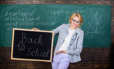 Bayan eğitimci sınıfta yeni öğretim yılı için hazır olun. Yeni okul sezon başında. Kadın öğretmen resmi elbise blackboard yazıt okula geri tutar. Yeni öğretim yılı öğretmen ağırlıyor