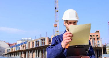 Koruyucu kask standı önünde bina ve vinç, adam. İş giyisi ve kask Oluşturucu inşaat alanında çalışır. Vinç denetleyicisi sorumlulukları kavramı. Kontrol inşaat süreci