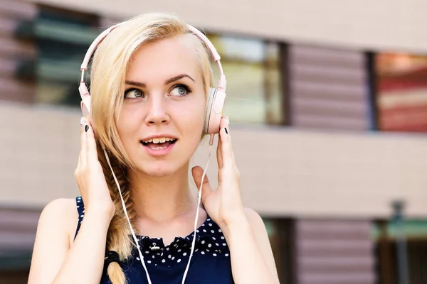 Jovencita escuchando audífonos musicales sobre fondo urbano, desenfocados. A una mujer con cara feliz le gusta la música. Concepto de música y ocio — Foto de Stock