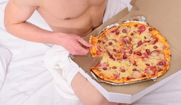 Guy naked covered pizza box sit bed bedroom offer you join him. Gastronomic satisfaction. Male courier sexy muscular torso holds pizza. Sexy courier delivers gastronomic satisfaction to your bed