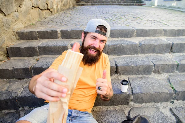 Hipster desfrutar de cachorro quente e beber xícara de papel. Conceito de cultura alimentar urbana. Hábitos nutricionais e lanches insalubres. Homem barbudo desfrutar de comida de rua fundo urbano. Hipster comer cachorro-quente enquanto relaxa escadas — Fotografia de Stock