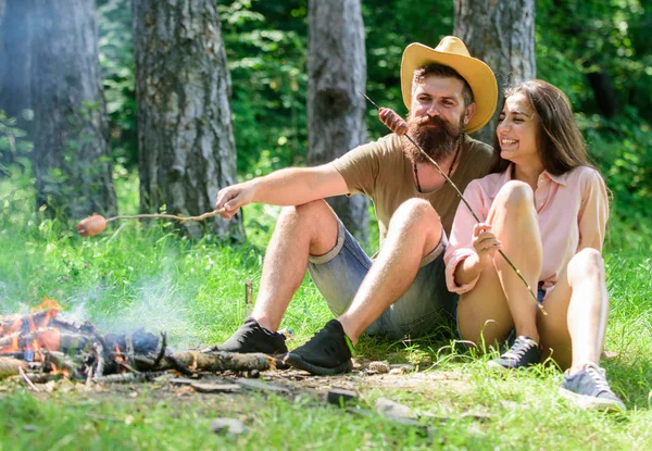 Kirándulás a piknik a hagyományos sült ételeket. Kemping és piknik. Csípő, és a lány pörkölés kolbász. Szeretet, kempingben pár erdei pörkölés kolbász. Pár készítsünk sült kolbász, snack jellegű háttér — Stock Fotó