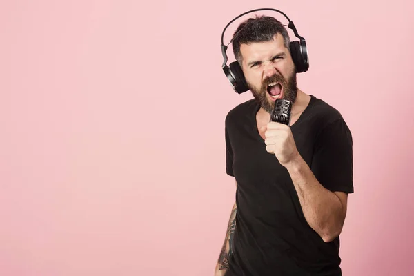 El hombre sostiene el micrófono en el fondo rosa, espacio de copia. Dj con barba usa auriculares. Concepto de música y ocio . — Foto de Stock
