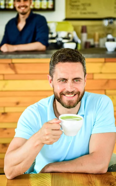 Many ways to enjoy coffee. Drink it black with milk or cream hot or cold. Add flavor or sweeteners. Man bearded guy drinks cappuccino wooden table cafe. Cafe visitor smiling face enjoy coffee drink