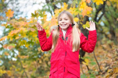 Neşeli kız öğrenci. Sıcak ceket açık yürüyüş çocuk sarı uzun saçlı. Kız kırmızı ceket mutlu Sonbahar Doğa Parkı tadını çıkarın. Çocuk giyim moda ceket kukuleta ile. Sonbahar giyim ve moda kavramı