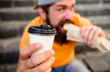 Man hipster have quick lunch sit stairs background. Paper cup coffee and hot dog street food traditional snack. He likes urban lunch. Delicious snack. Coffee to go and street food choice of youth clipart