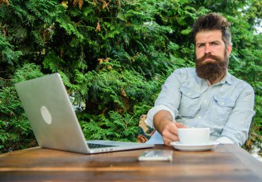 Sakallı adam hipster yapmak için kahve içmek duraklatmak ve dizüstü bilgisayar ile oturup süre düşünüyorum. Dinlenmek için mola. Adam kahve rahatlatıcı Teras yeşil dallar arka plan içer. Hoş bir an. Düşünmek için zaman ayırın