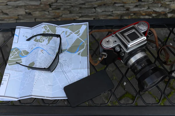 Travel tourist map and other equipment. Retro camera, sunglasses and mobile phone lying on city guide. Travellers kit concept. — Stock Photo, Image