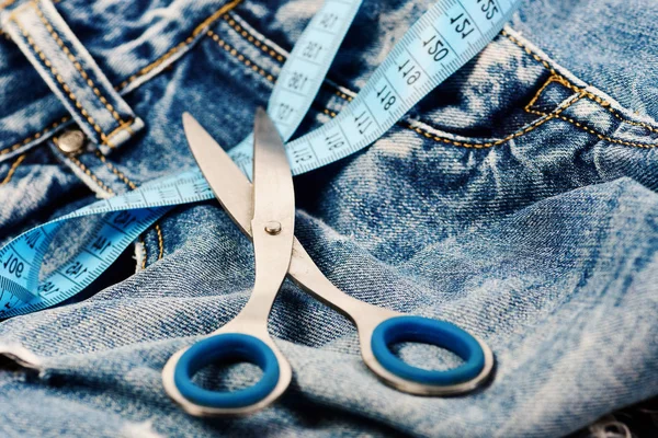 Tesoura de metal e fita métrica azul em jeans. Ferramentas de alfaiataria em tecido denim, foco seletivo — Fotografia de Stock