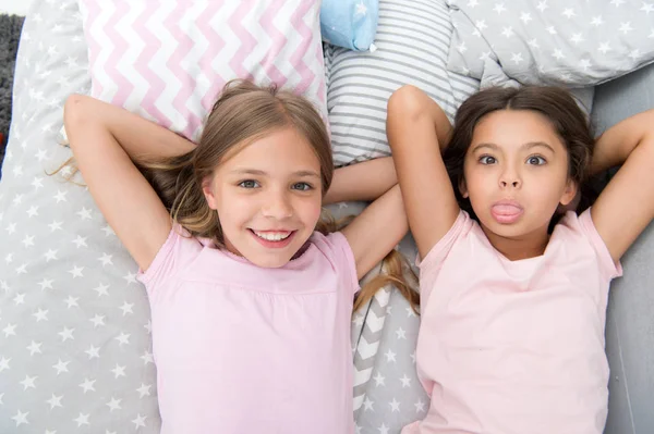 Best friends forever. Girls children lay on bed with cute pillows top view. Pajamas party concept. Girls in playful mood with grimace face. Friends children having fun together and feel comfortable