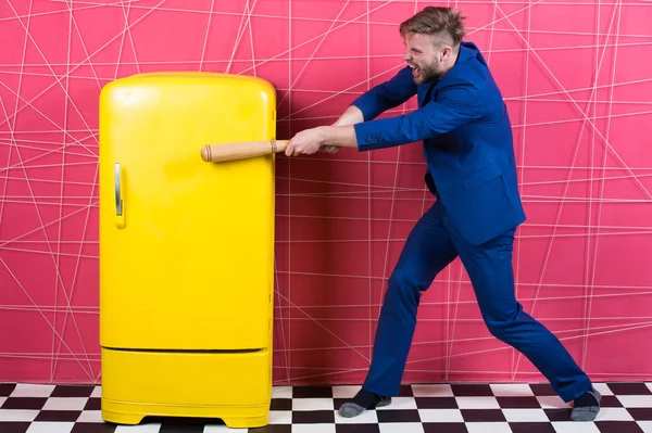 Man formal elegant suit beat with wooden bat retro vintage yellow refrigerator. Bachelor hungry want eat near fridge. Bright fridge household appliances. Hunger and appetite. Hungry attack concept