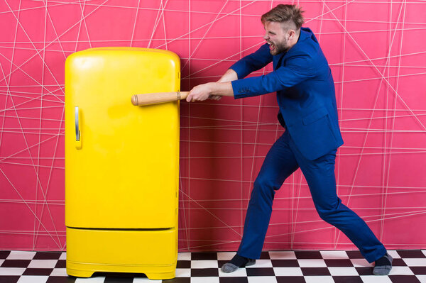 Мужчина формальный элегантный костюм бить деревянной летучей мыши ретро-винтажный желтый холодильник. Голодный холостяк хочет есть возле холодильника. Яркий холодильник бытовой техники. Голод и аппетит. Концепция голодной атаки