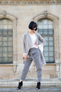 Şık kıyafet. Dışarıda poz veren modaya uygun bir kadın. Esmer kız saç stili şık görünüyor. Kısa saç stili, şehir mimarisi geçmişi olan şık bir kız.