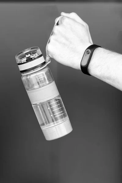 Hand holds sporty bottle of water or sport drink, brown background. Bottle of water in male hand with smart watch or pedometer. Sporty drink in bottle with strap. Sport and water balance concept