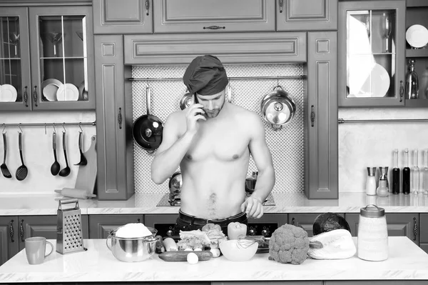 El hombre habla por teléfono móvil en la cocina. Cocine en sombrero de chef con torso sexy en la mesa. Menú vegetariano y dieta saludable. Preparación de alimentos y recetas de cocina. Comunicación y nuevas tecnologías — Foto de Stock