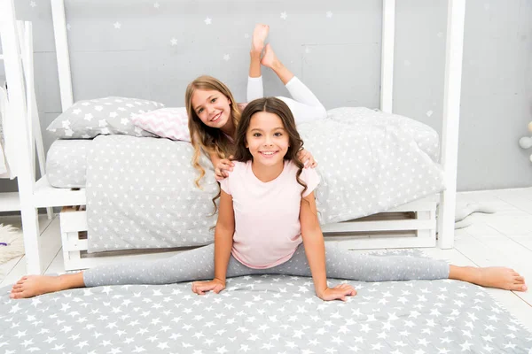 Hora de estirar la noche. Linda práctica de gimnasta dividida con un amigo. Niña sentada dividida en dormitorio. Amigos gimnastas se apoyan mutuamente. Estilo de vida del régimen deportivo. Chica niño lindo pijama estiramiento — Foto de Stock