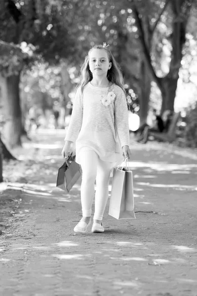 Petite princesse avec couronne sur cheveux longs blonds. Fille avec des sacs à provisions marcher dans le parc. Acheteur enfant en vêtements de mode en plein air. Enfant avec des sacs en papier en été. Shopping en vente et achat — Photo