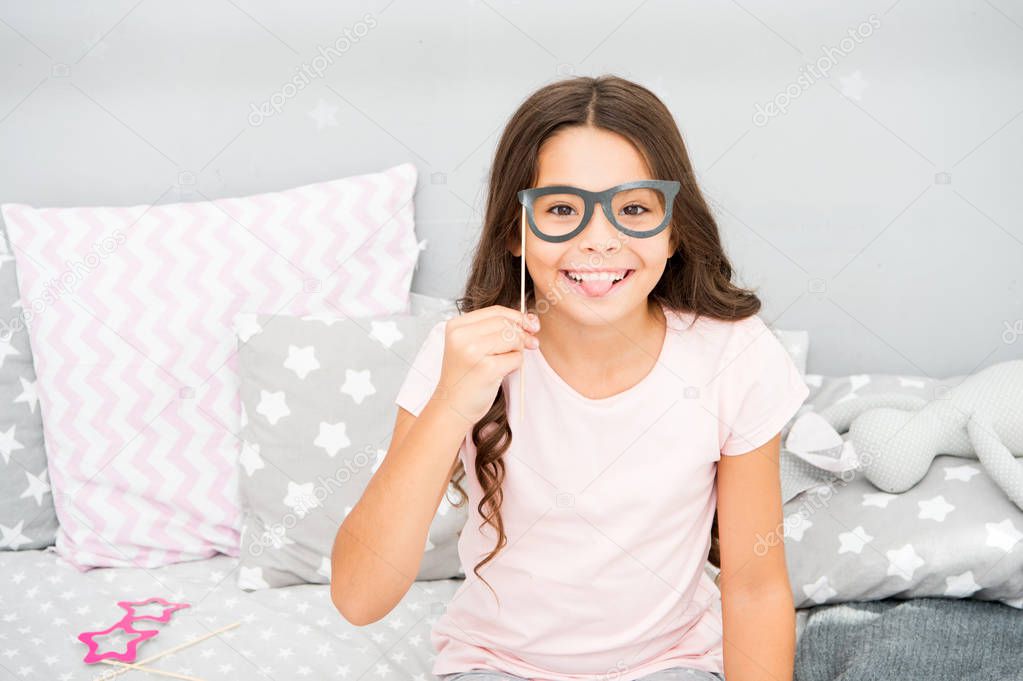 Girl child posing with cute grimace show tongue photo booth props. Eye health and vision concept. Girl having fun pajamas party. Kid cute and cheerful posing with eyeglasses accessories