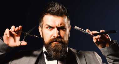 Sakallı adam tıraş bıçağı ve makas tutuyor.