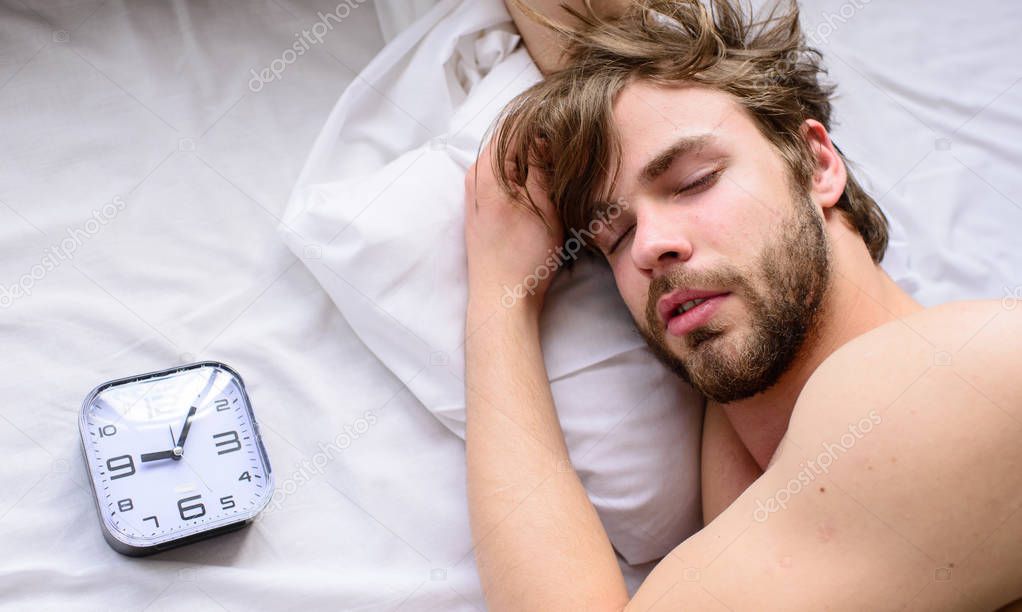 Oversleep problem. Man unshaven sleepy face lay pillow alarm clock top view. Guy sleep missed alarm clock ringing. Manage proper regime tips. Toughest part of morning simply getting out of bed