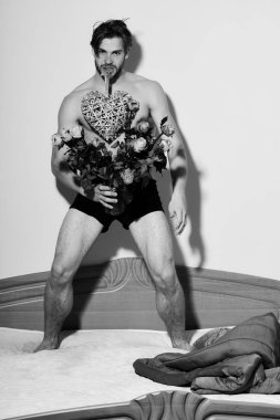 Yakışıklı, sakallı, seksi, maço sakallı adam kırmızı battaniyenin yanında iç çamaşırıyla duruyor. Elinde turuncu güller ve dişlerinde süslü sevgililer günü kalbi var..