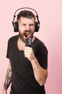 Adam pembe arka planda şarkı söylüyor. Sakallı DJ kulaklık takıyor..