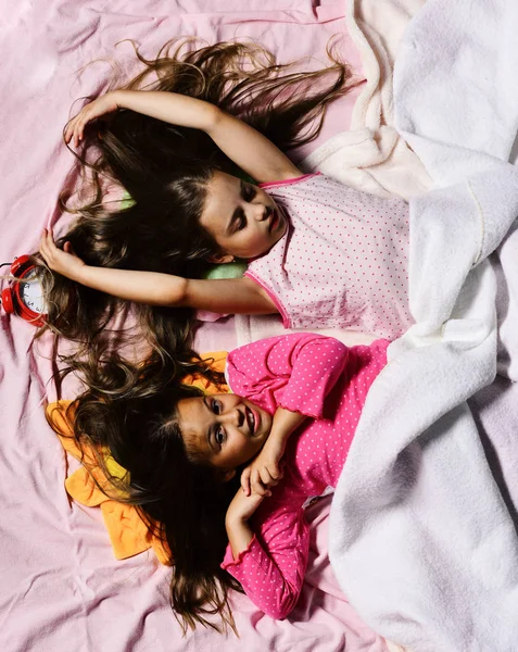 Schoolgirls in pink pajamas wallow on colorful pillows, top view.