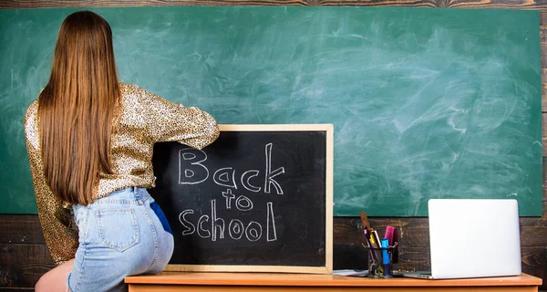 Girl denim skirt breaking school clothing rules. Back and buttocks student near chalkboard. School dress code. Student teacher mini skirt sexy buttocks sit table blackboard inscription back to school