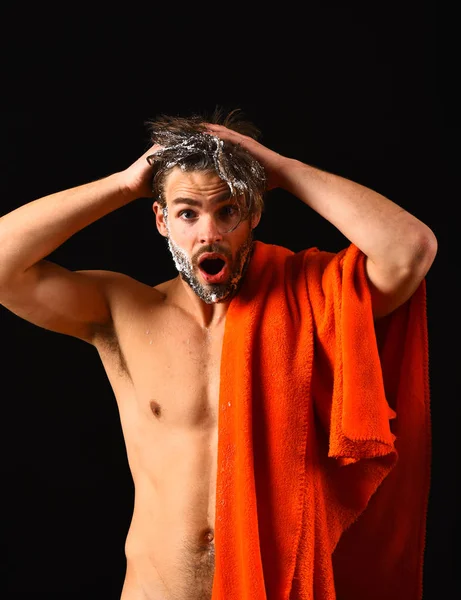 Man bearded tousled hair covered with foam or soap suds. Wash off foam with water carefully. Need take shower. Man with orange towel ready to take shower. Macho attractive nude guy black background — Stockfoto