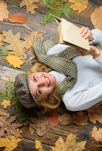 Girl blonde lay wooden background with leaves. She likes detective genre. Woman lady in checkered hat and scarf read book. Girl in vintage outfit enjoy literature. What to read in autumn book list