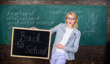 Öğretmen yeni öğretim yılı ağırlamaktadır. Yeni okul sezon başında. Bayan eğitimci sınıfta yeni öğretim yılı için hazır olun. Kadın öğretmen resmi elbise blackboard yazıt geri okula tutar