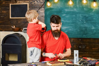 Baba, anne-baba Okulu atölyesinde farklı araçları kullanmaya sakal öğretim oğlu ile. Evlat, çocuk neşeli cıvata veya vida ve kask, baba ile handcrafting sırasında eğlenmek tutar. Tamirci kavramı.