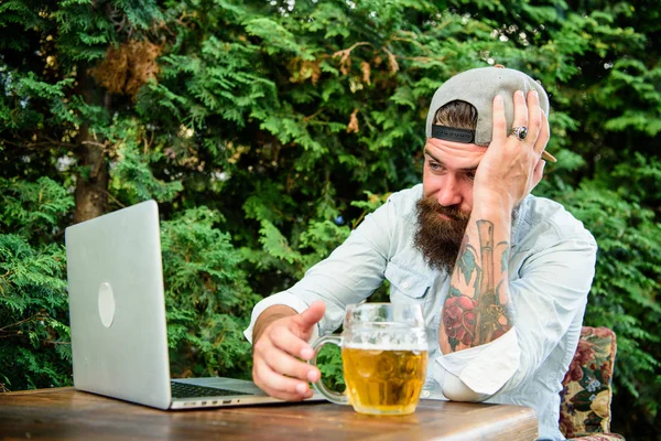 Disappointed with game result. Brutal man leisure with beer and sport game. Fan watch stream online while sit terrace outdoors drink beer. Football fan bearded hipster watch game on laptop screen
