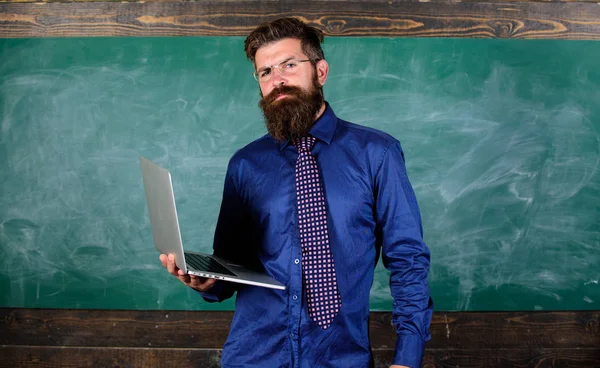 Educación en tecnología digital. Hipster profesor usar gafas y corbata sostiene portátil. Profesor barbudo hombre con un moderno fondo de pizarra portátil. Educación en línea. Educación tecnológica moderna — Foto de Stock