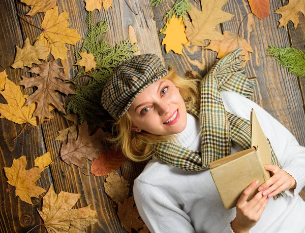 Fall and autumn season. Woman lady in checkered hat and scarf read book. She likes detective genre. Girl in vintage outfit enjoy literature. Girl blonde lay wooden background with leaves top view