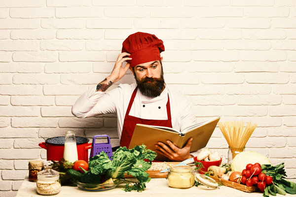 Cook with confused face in uniform sits by vegetables