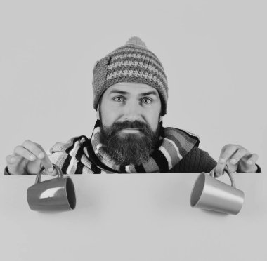 Sıcak şapkalı adam kahverengi ve yeşil bardağı tutuyor.