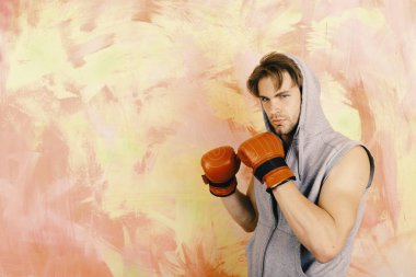 Gri kolsuz kapüşonlu adam kırmızı boks eldiveni giyiyor.