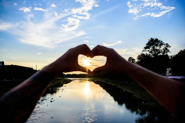 Idea honeymoon travel. Sunset sunlight romantic atmosphere. Hands heart gesture symbol of love and romance. Heart gesture in front of sunset above river. Honeymoon summer resort. Romantic date ideas