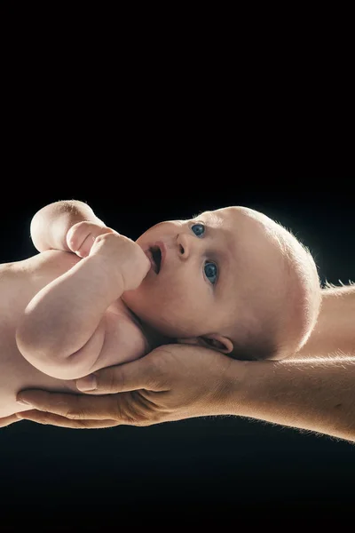 Bambino tenuto da mani di genitori su sfondo nero . — Foto Stock