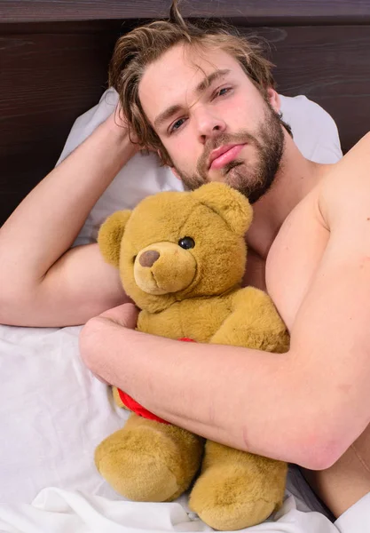 男人胡子胡子的脸放松与喜爱的泰迪熊。美梦的概念。男人英俊的家伙放松床拥抱泰迪熊玩具。童年的甜蜜回忆。家伙躺在白色的床单与玩具 — 图库照片